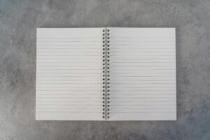 Top-down view of an open spiral notebook with lined pages on a textured gray surface.