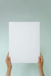 Close-up of hands holding a blank white paper against a neutral background, perfect for mockups.