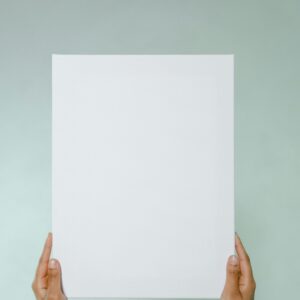 Close-up of hands holding a blank white paper against a neutral background, perfect for mockups.