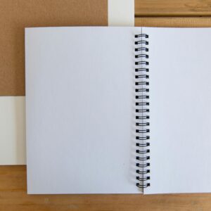 Open white spiral notebook on a wooden desk for simple and minimalist design projects.