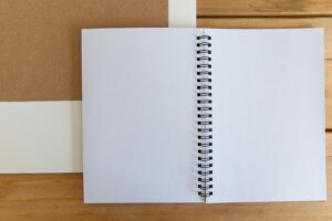 Open white spiral notebook on a wooden desk for simple and minimalist design projects.