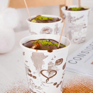Appetizing chocolate drinks topped with green garnish in artistic paper cups set on a table.