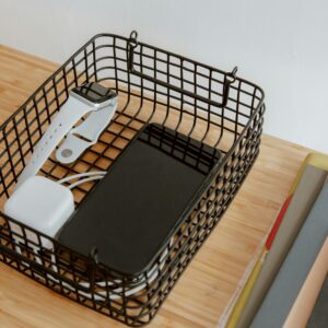 Organized workspace with tech gadgets in a wire basket on a wooden desk.