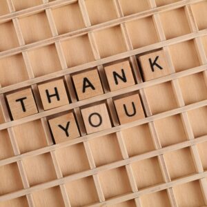 Wooden letter tiles spelling 'thank you' on a grid background, perfect for gratitude themes.