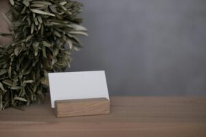 A blank business card displayed on a wooden holder with a natural plant backdrop, perfect for branding visuals.