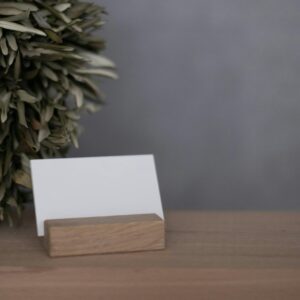 A blank business card displayed on a wooden holder with a natural plant backdrop, perfect for branding visuals.