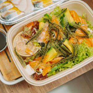 Delicious seafood salad with fresh seaweed, avocado, and salmon in a biodegradable container.