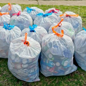 Plastic trash bags filled with recyclable materials on grass, raising recycling awareness.