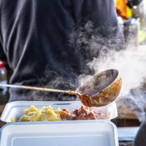 Street food vendor serving steaming hot food into a container, showcasing delicious and tasty meals.