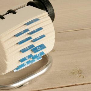 A close-up of a traditional Rolodex with alphabet tabs on a wooden desk.
