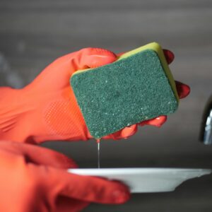 Close-up of hands in rubber gloves using a sponge to wash a ceramic plate over a sink.