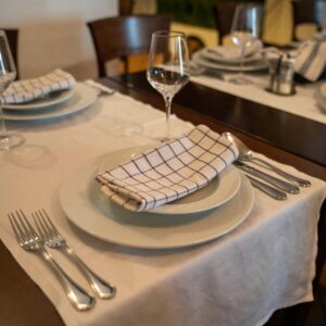 Elegant dining table with white tablecloth, cutlery, and checkered napkin in a cozy restaurant setting.