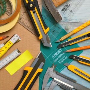 A vibrant flat lay of various office and craft tools, including knives and tapes, on a wooden surface.