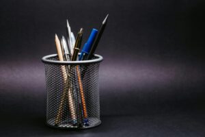 Close-up of various pens and pencils in a mesh holder against a black background.