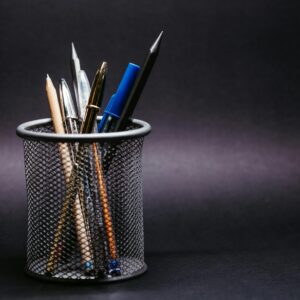 Close-up of various pens and pencils in a mesh holder against a black background.