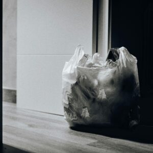 A dimly lit room containing a plastic bag filled with trash, emphasizing waste and recycling.
