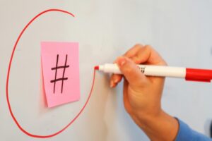 Close-up of hand drawing a circle around a hashtag on a sticky note with a red marker.