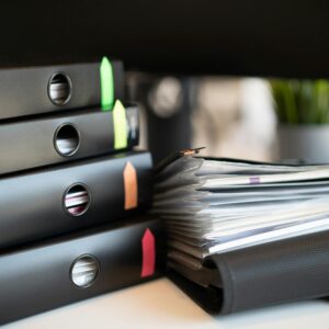 Stack of colorful ring binders and documents on a modern office desk setting.