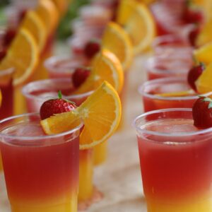 Colorful tropical cocktails garnished with oranges and strawberries in clear cups.