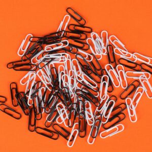 A pile of monochrome paper clips on a vibrant orange background, showcasing contrast and color.