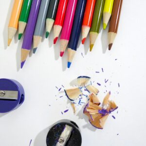 Bright colored pencils and sharpeners with shavings on a white surface.