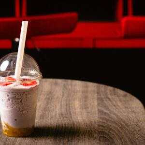 Delicious strawberry milkshake with a straw in a clear cup on a rustic wooden table, perfect for a summer treat.