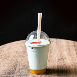 A blue milkshake in a plastic cup with dome lid and straw on a wooden table.