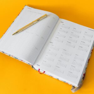 Open planner for 2023-2025 with a golden pen on a vibrant yellow background, perfect for organizing and planning.