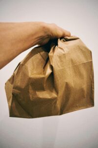 A hand holding a crumpled brown paper bag with a plain white background.
