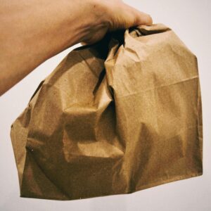A hand holding a crumpled brown paper bag with a plain white background.