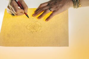 Hands tracing a floral design on backlit paper, showcasing artistic craftsmanship.
