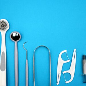 Flat lay of dental care tools including toothbrushes, dental mirror, and floss sticks on blue background.