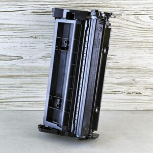 Close-up of a black printer toner cartridge against a rustic wooden background, side view.