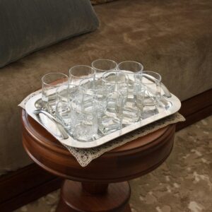 A silver tray with eight clear glasses on a wooden table beside a sofa.