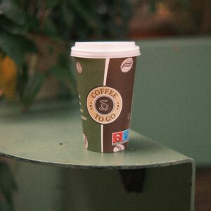 A warm coffee in a paper cup on a green table outdoors. Perfect for on-the-go caffeine lovers.