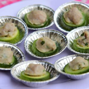 Delightful gourmet appetizers featuring meatballs on fresh zucchini slices in foil cups.