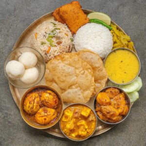 A traditional Indian thali featuring rice, curry, dal, and more, on a brass plate.