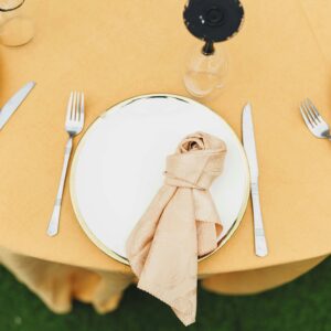 Overhead view of a table setting with a yellow tablecloth, white plates, and neatly folded napkins.
