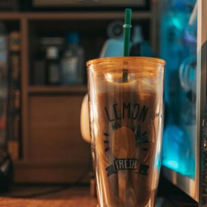 Transparent tumbler with lemon-themed design and straw placed indoors against aesthetic backdrop.