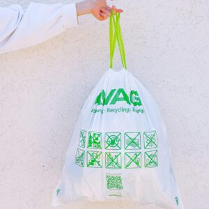 A person holding a white recycling bag with green symbols against a white wall, promoting sustainability.