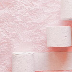 Toilet paper rolls arranged on a pink textured background for a clean, minimalist look.