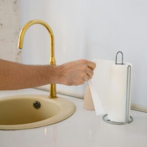 A bathroom sink with a golden faucet and hand reaching for a paper towel in a clean setting.
