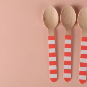 Three eco-friendly wooden spoons with striped handles on a minimalist pink background.