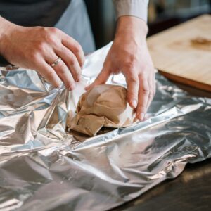 Close-up of a chef's hands wrapping food ingredients in foil for cooking.