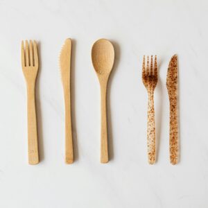 Top view of wooden and plastic cutlery placed in row on white marble table