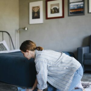 A woman cleaning the floor in a cozy bedroom using a cloth on a carpet.