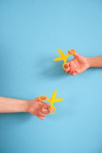 Two hands holding yellow scissors against a blue backdrop, featuring ample copy space.