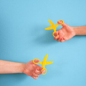 Two hands holding yellow scissors against a blue backdrop, featuring ample copy space.