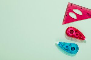 Top view of colorful correction tapes and a triangle ruler on a pastel green background.