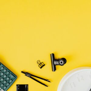 Flat lay of office supplies on a bright yellow background with ample copy space.